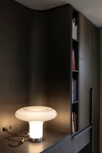 極簡設計，擺放一盞流線型白色桌燈，搭配金屬燈座，置於現代深色木櫃前方