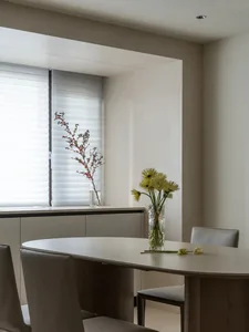 Modern dining room with minimalist furniture and decor, including a round table, chairs, and fresh flowers in a vase by the w