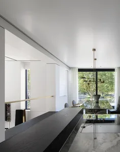 A modern living space featuring a minimalist interior with white walls and mixed materials, including a black dining table se
