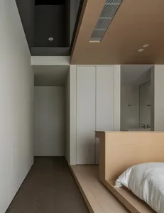 Modern minimalist bedroom featuring light wooden accents, white bedding, and sleek white wardrobe.