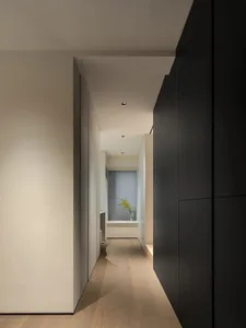 A hallway with black wooden walls and floor, light coming through a window with blinds.