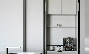 A minimalist modern white kitchen with sleek cabinets and an espresso machine on the countertop.