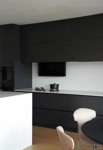 A modern, minimalist kitchen with black cabinets, stainless steel countertops, and a light wood floor.