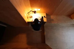 A minimalist workspace with wooden walls, a desk, and a person working on a project.