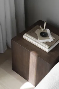A wooden bedside table featuring books and a small desk lamp, placed in a modern bedroom setting.