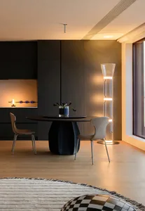 Modern dining room featuring a sleek black table, minimalist chairs, and contemporary floor lamp with illuminated glass tubes