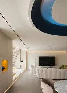 A modern living room with a curvilinear blue ceiling feature and concrete floor.