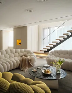 Modern living room featuring plush white sofas with yellow accents, a black coffee table, and a staircase in the background.