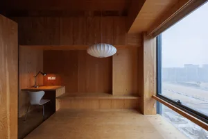 A modern office space features a wooden desk and chair with a pendant light hanging above. The floor and walls are made of wo
