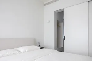 A minimalist bedroom with a bed, white bedding, and a closed closet.