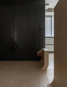 A minimalist entryway with a black glass wall and a wooden bench on white flooring