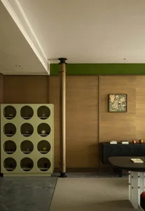 Modern interior design of a living room featuring a green shelving unit, wooden columns, and a black cabinet.