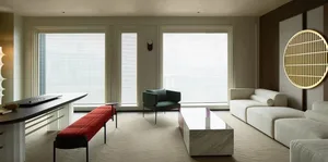A modern living room featuring marble coffee table, upholstered furniture, and large windows with blinds.