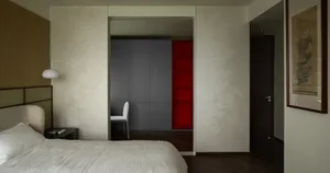A minimalist bedroom with a white bed, white walls, and white fabric headboard, featuring a wooden floor.