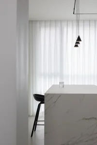Modern minimalist kitchen with a white marble countertop and a sleek, black chair.