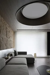 The image depicts an industrial-style living room with a modern concrete wall and a ceiling light fixture.