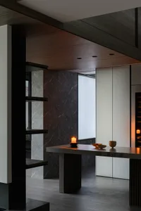 Modern dining room with marble walls and table, featuring a candle and minimalist decor.