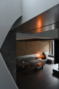 A modern living room with stone and cement walls, a gray sectional sofa, and a wooden table with a bowl.