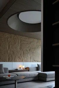 A contemporary living room with stone and concrete materials, featuring a round skylight and a comfortable sectional sofa.