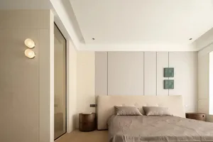 A minimalist bedroom featuring a bed with a beige headboard, grey linens, and a wooden floor, with a white and beige wall, an