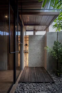An industrial outdoor shower area with concrete walls and a wooden deck surrounded by rocks and plants.
