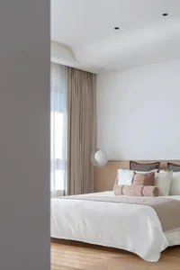 Modern minimalist bedroom with neutral-toned bedding, pillows, and curtains.