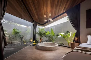 A minimalist bedroom featuring wooden elements and a circular stone bathtub surrounded by plants.