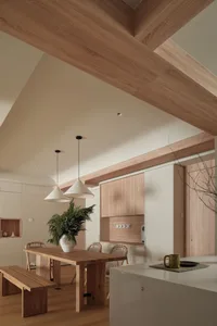 A modern, minimalist kitchen with light wood finishes and clean lines, featuring a wooden dining table, bench seating, and pe