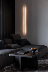 A minimalist living room featuring concrete furniture, a book, a bowl of fruits, and a hanging light fixture.