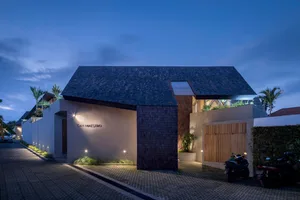 Modern house with concrete exterior at dusk with palm trees and blue skies.