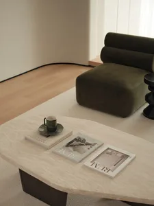 A modern living room with a green upholstered sofa, two magazines, and a ceramic mug on a beige tile table.