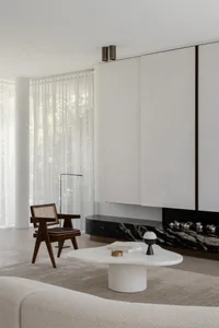 Minimalist living room featuring marble coffee table, concrete fireplace, and modern chair with woven seat.
