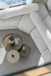A minimalist living room featuring neoprene furniture, a round glass coffee table, and a large window allowing natural light 