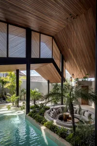 Modern residential interior with a wooden ceiling, curved roof, circular seating area with cushions, and a pool surrounded by