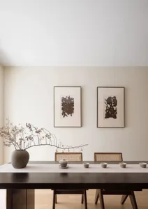 Modern dining room with wooden table and cane-back chairs, minimalistic art on the wall, and a vase with dried branches.