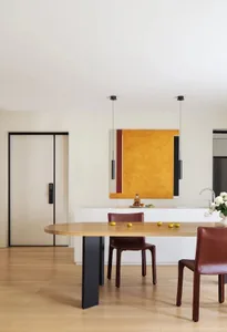 Modern dining room featuring a wooden table with metal legs, two brown leather chairs, and a minimalist orange abstract paint