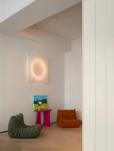 A cozy living room with plush cushions and a wooden floor, featuring a sunburst light fixture and colorful artwork.