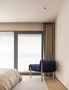 Minimalist bedroom with a textured blue armchair, white blinds, and wooden flooring.