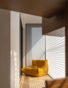 Modern living room featuring a yellow upholstered chair on a wooden floor with sunlight streaming through horizontal blinds.
