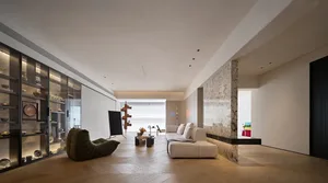 Modern minimalist living room featuring a white couch, marble fireplace, glass coffee table, and wooden floor.