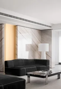 Modern minimalist living room featuring marble walls, concrete flooring, and black leather couch.
