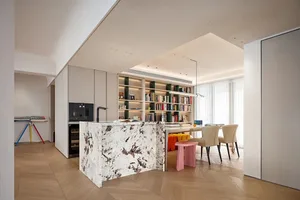 A modern residential kitchen with a granite countertop and bookshelves filled with books.