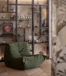 A textured lounge chair with a green upholstery in a modern living room with a display cabinet.