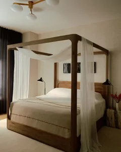 A minimalist bedroom with a wooden bed frame, white curtains, and black table lamps on either side of the bed.