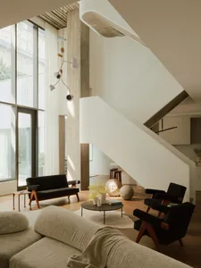 A minimalist living room featuring concrete columns, a white staircase, and a wooden floor.
