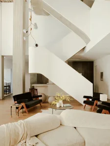 A modern living room with neutral leather furniture, a circular coffee table with white and green plants, and a spiral stairc
