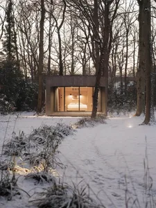A minimalist cabin with wood and glass exterior in a snowy forest setting.
