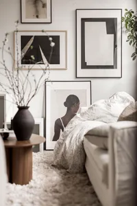 A minimalist living room with a white couch, a round wooden table with a black vase, and a variety of black and white framed 