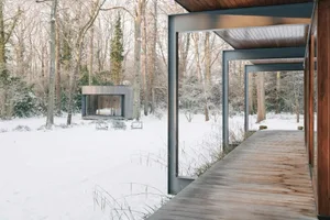 現代極簡住宅外觀，木質步道穿梭於雪景與樹木之間。