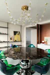 A modern dining room featuring a round marble table surrounded by green and blue high-back chairs.